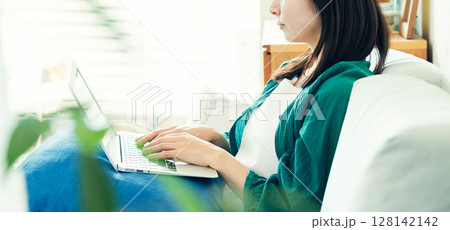 リビングでパソコンを使う若い女性 リビングでパソコンを使う若い女性 128142142