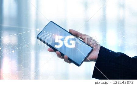Hand holding smartphone with 5G icon and global network interface, representing high-speed wireless technology, digital connectivity, IoT, and future communication concept. communication network. Hand holding smartphone with 5G icon and global network interface, representing high-speed wireless technology, digital connectivity, IoT, and future communication concept. communication network. 128142872