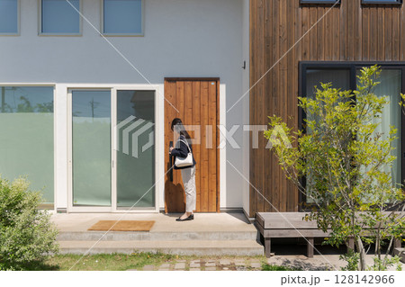 玄関のドアを閉めるスーツの女性 128142966