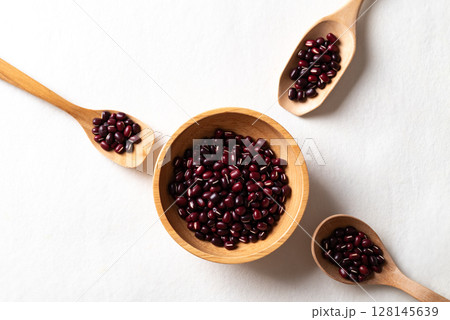 Top view of raw Azuki beans or red mung beans in wooden bowl and spoon on white background Top view of raw Azuki beans or red mung beans in wooden bowl and spoon on white background 128145639