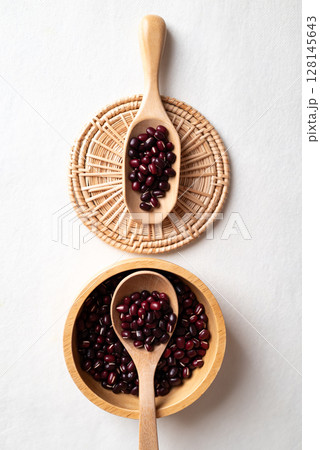 Top view of raw Azuki beans or red mung beans in wooden bowl and spoon on white background Top view of raw Azuki beans or red mung beans in wooden bowl and spoon on white background 128145643