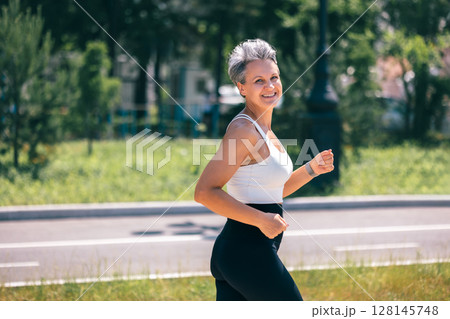 Smiling Mature Woman Jogging in Park on a Sunny Day, Embracing Healthy Active Lifestyle Smiling Mature Woman Jogging in Park on a Sunny Day, Embracing Healthy Active Lifestyle 128145748