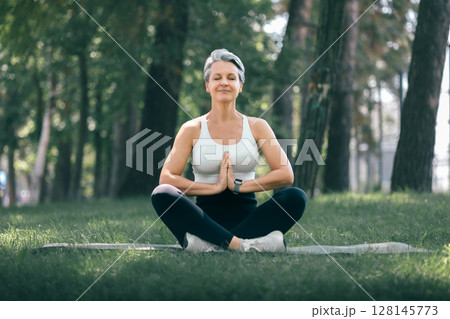 Mature Woman Meditating with Hands in Namaste Pose Outdoors in a Peaceful Forest Setting Mature Woman Meditating with Hands in Namaste Pose Outdoors in a Peaceful Forest Setting 128145773