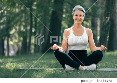 Happy Mature Woman Meditating Outdoors in Nature During Morning Yoga Session in the Park 128145781