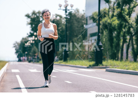Confident Mature Woman Jogging Outdoors on a Sunny Day in Sportswear and Smartwatch 128145783
