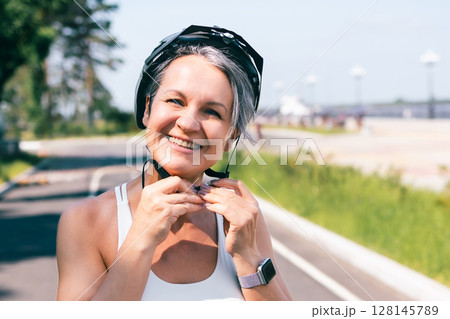 Smiling active woman fastening bicycle helmet before cycling on a sunny outdoor trail Smiling active woman fastening bicycle helmet before cycling on a sunny outdoor trail 128145789