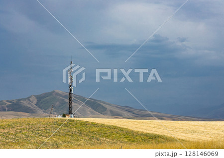Telecommunication tower on hill, near agricultural field. Countryside landscape 128146069