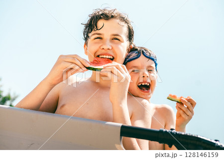 Two happy boys laugh and enjoy juicy watermelon slices on a sunny summer day at the swimming pool Two happy boys laugh and enjoy juicy watermelon slices on a sunny summer day at the swimming pool 128146159