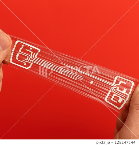 Hands stretching transparent flexible electronic circuit with printed conductive lines  128147544