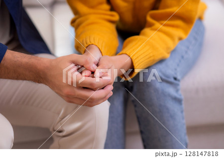 Closeup hand caring man comforts sad woman with gentle embrace sitting on sofa in living room. 128147818