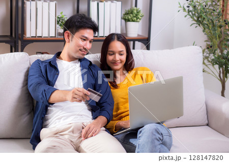 Happy asian couple using laptop and credit card for online shopping together in living room. Happy asian couple using laptop and credit card for online shopping together in living room. 128147820