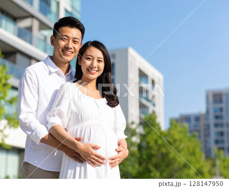 アジア人の若い妊婦と夫が笑顔で高層マンションの前でポーズ アジア人の若い妊婦と夫が笑顔で高層マンションの前でポーズ 128147950