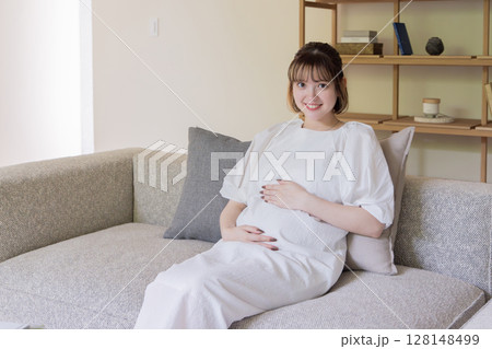 お腹を抑えソファに座る妊婦 128148499
