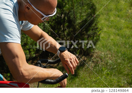 Cyclist checking smartwatch, geolocation, timer, distance, pulse or fitness progress in apps after riding. Close up. Summer activity. Cyclist checking smartwatch, geolocation, timer, distance, pulse or fitness progress in apps after riding. Close up. Summer activity. 128149864