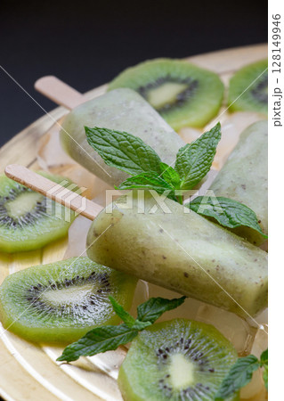 Kiwi ice cream popsicles are beautifully presented atop sliced kiwi fruits. Fresh mint leaves add a vibrant touch, enhancing the desserts visual appeal and flavor. Kiwi ice cream popsicles are beautifully presented atop sliced kiwi fruits. Fresh mint leaves add a vibrant touch, enhancing the desserts visual appeal and flavor. 128149946