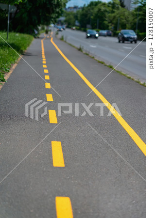 Bicycle lane marked with yellow line runs along city sidewalk. Urban bike path marked with yellow dashed and solid lines along gray asphalt surface. Concept of transportation, safety, active mobility Bicycle lane marked with yellow line runs along city sidewalk. Urban bike path marked with yellow dashed and solid lines along gray asphalt surface. Concept of transportation, safety, active mobility 128150007