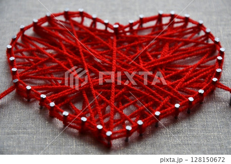 Red heart string art made with tangled yarn on metal nails on canvas background 128150672