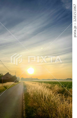 Experience the serene beauty of a vivid sunrise over a peaceful country road and fields 128151067