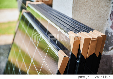 Close-up new solar panels with protective cardboard corners, ready for installation. Renewable energy technology, green living, and the implementation of solar power in residential areas. Close-up new solar panels with protective cardboard corners, ready for installation. Renewable energy technology, green living, and the implementation of solar power in residential areas. 128151107