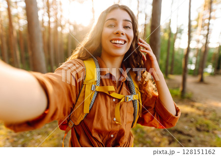Beautiful woman taking picture of herself while walking in sunny forest. Selfie in nature. Adventure 128151162