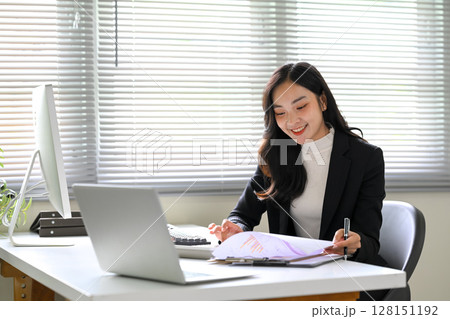 Young businesswoman reviewing financial reports while working at her desk in a bright office 128151192