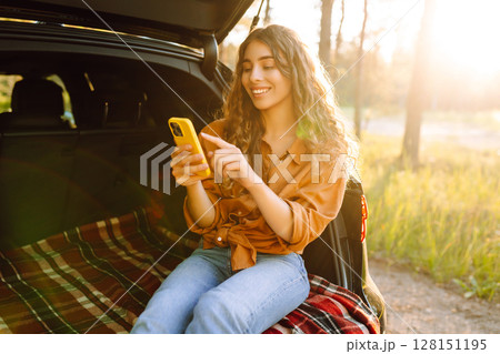 Young woman enjoys a sunny day outdoors while sitting in her car. Travel, weekend, nature, relax 128151195