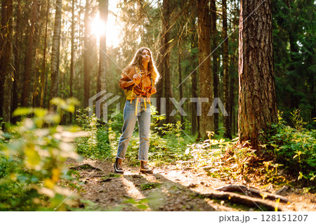 Tourist woman hiking alone in thick autumn forest. Stylish female looks for pathway among trees. 128151207