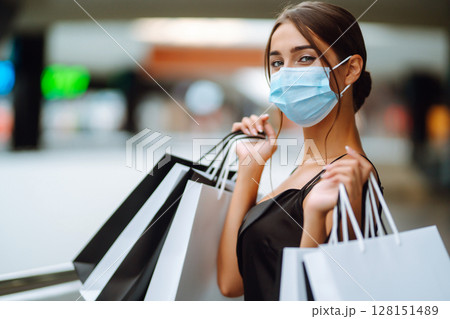 Fashionable woman in protective medical mask with shopping bags walking in the mall. Covid-19. Fashionable woman in protective medical mask with shopping bags walking in the mall. Covid-19. 128151489