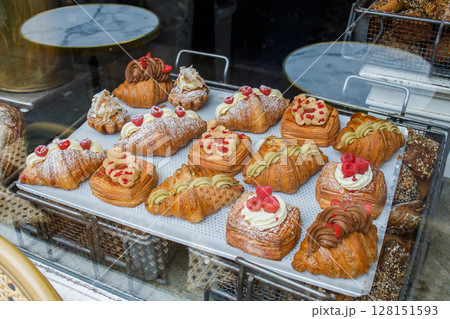 Danish pastry on a a cafe showcase behind the window: view from the street. Tasty buns and croissants in a bakery in Copenhagen, Denmark. Danish pastry on a a cafe showcase behind the window: view from the street. Tasty buns and croissants in a bakery in Copenhagen, Denmark. 128151593