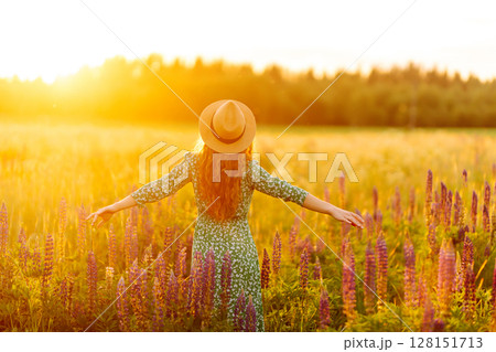 Stylish woman in a straw hat with a bouquet of flowers on a field with lupins. Lifestyle concept. 128151713
