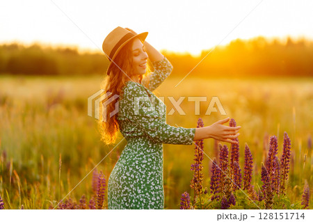 Stylish woman in a straw hat with a bouquet of flowers on a field with lupins. Lifestyle concept. 128151714