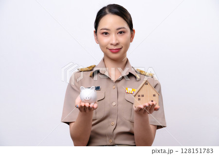 Young Thai Asian Teacher in the uniform is holding the piggy bank and wooden house Young Thai Asian Teacher in the uniform is holding the piggy bank and wooden house 128151783