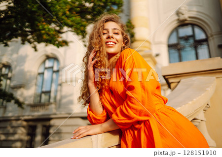 Young woman posing against backdrop of urban landscape in bright orange dress. Concept of lifestyle. 128151910
