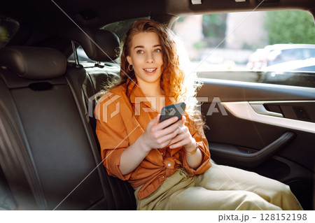 A young woman with a smartphone chats in the back seat of a car. Transport concept. Lifestyle. 128152198