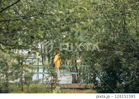 man in orange hoodie standing on small wooden bridge with backpack, lush green foliage and trees near water, eco tourism, travel agency, outdoor adventure company man in orange hoodie standing on small wooden bridge with backpack, lush green foliage and trees near water, eco tourism, travel agency, outdoor adventure company 128152395