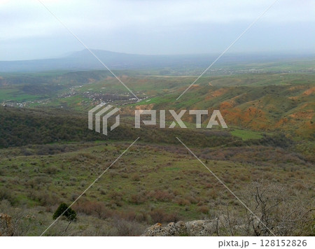 A sprawling valley with rolling green hills, a small village nestled in the distance, and faint mountains under a cloudy sky, capturing a peaceful rural landscape A sprawling valley with rolling green hills, a small village nestled in the distance, and faint mountains under a cloudy sky, capturing a peaceful rural landscape 128152826