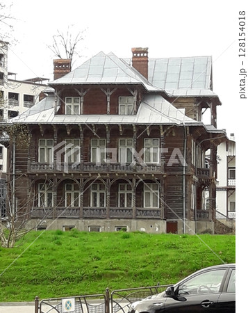 A Wooden House with a Steep Roof and Balconies Surrounded by Grass and a Parked Car 128154018