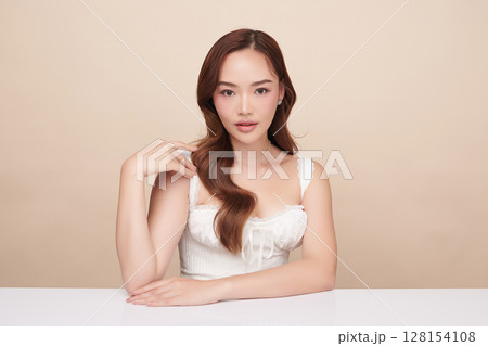 A beautiful young Asian woman with clean, fresh skin against a beige background. Skincare, facial treatment, cosmetology, beauty, and spa. An elegant portrait of an Asian woman. 128154108