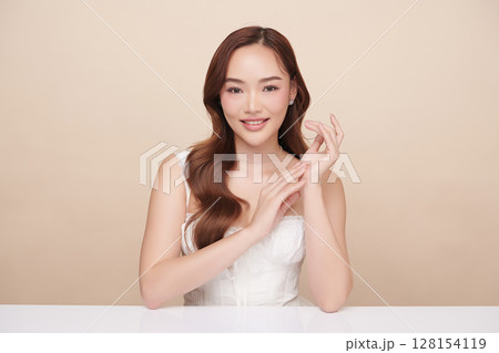 A beautiful young Asian woman with clean, fresh skin against a beige background. Skincare, facial treatment, cosmetology, beauty, and spa. An elegant portrait of an Asian woman. 128154119