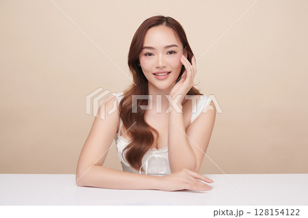 A beautiful young Asian woman with clean, fresh skin against a beige background. Skincare, facial treatment, cosmetology, beauty, and spa. An elegant portrait of an Asian woman. 128154122