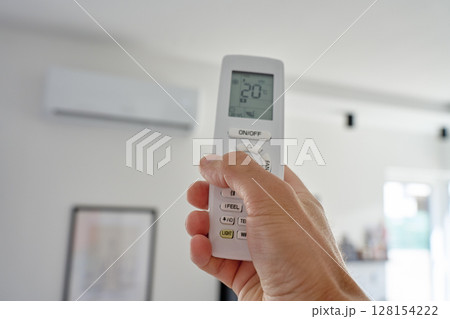 Hand using remote control to adjust temperature on air conditioner Hand using remote control to adjust temperature on air conditioner 128154222