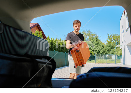 Man placing suitcase into car trunk before summer trip 128154237