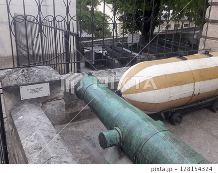 Historic Display of a Green Cannon and Striped Torpedo Behind a Black Iron Fence 128154324