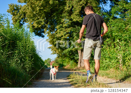 Man walking with small dog on countryside path in summer 128154347