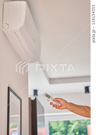 Hand using remote control to adjust temperature on air conditioner at home 128154355
