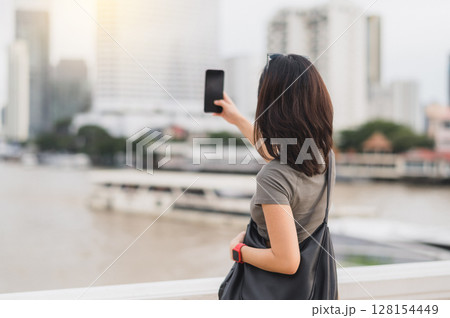 Happy solo southeast asian woman blogger and teenager take photo with smartphone. world travel explorer local cultural experience tourism concept Asia. Wait for express boat Chao Phraya river Happy solo southeast asian woman blogger and teenager take photo with smartphone. world travel explorer local cultural experience tourism concept Asia. Wait for express boat Chao Phraya river 128154449