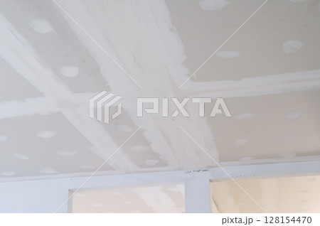 Building interior renovation features gypsum board ceiling plastering. Electrical wire visible near seams. Careful smoothing prepares edges for smooth ceiling surface Building interior renovation features gypsum board ceiling plastering. Electrical wire visible near seams. Careful smoothing prepares edges for smooth ceiling surface 128154470