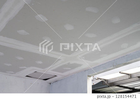 Interior renovation progress building smooth gypsum board ceiling edges. Plastering complete on ceilings showing precise work. Electrical wire visible reflecting effort towards finishing Interior renovation progress building smooth gypsum board ceiling edges. Plastering complete on ceilings showing precise work. Electrical wire visible reflecting effort towards finishing 128154471