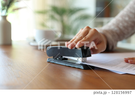 Closeup of a woman hand stapling papers on a table at home 128156997