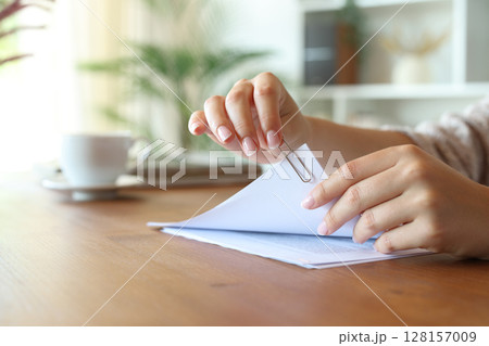 Woman hand putting a paper clip on document sheets at home Woman hand putting a paper clip on document sheets at home 128157009